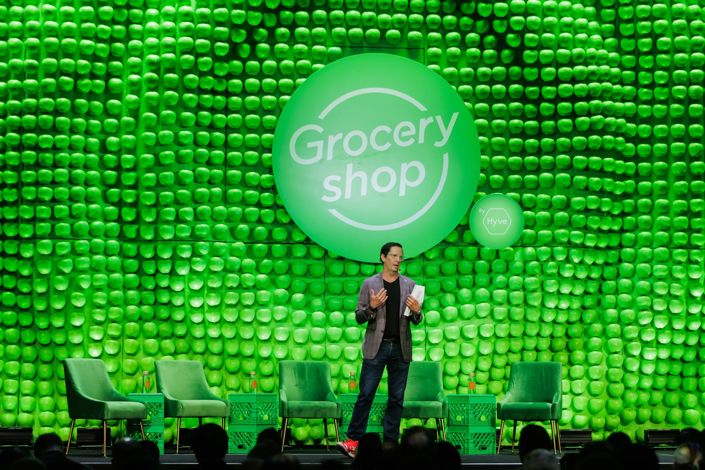 Groceryshop 2025 Greenlight Stage, an apple-pattern wall with crate side tables